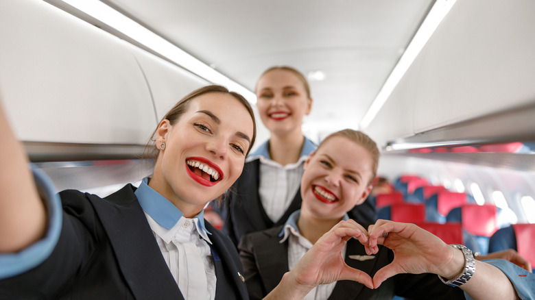Three flight attendants smiling for a photo on an empty plane.