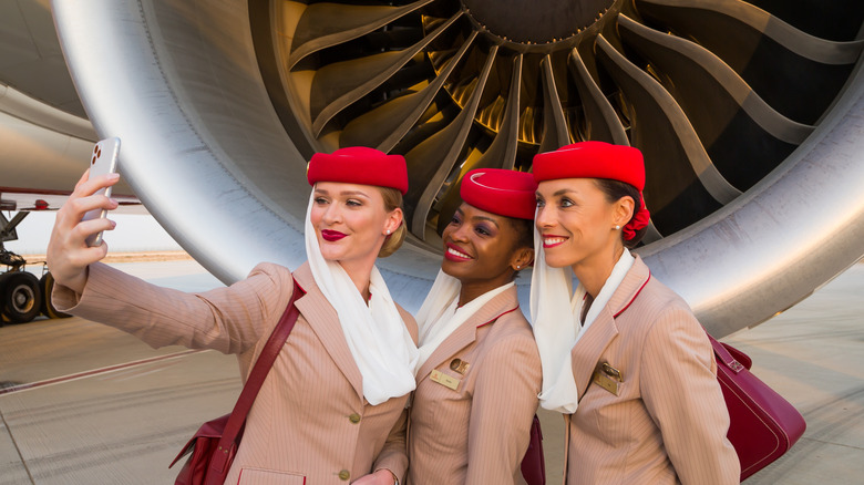 Three Emirates Airlines flight attendants taking a selfie in front of a plane engine.