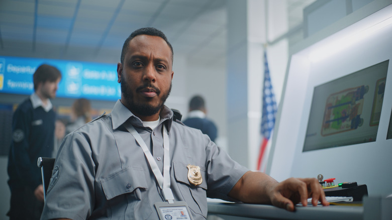A TSA agent on the job, sitting inside an airport next to a scanning device screen