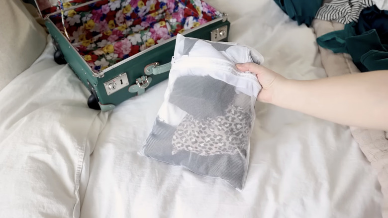 Hand holding a mesh laundry bag filled with clothes next to luggage