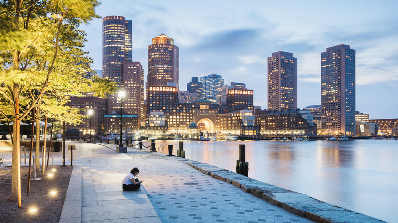 A woman checks her phone alone on the waterfront in Boston, Massachusetts