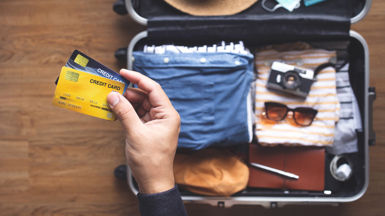 Someone holding credit cards in front of a packed suitcase
