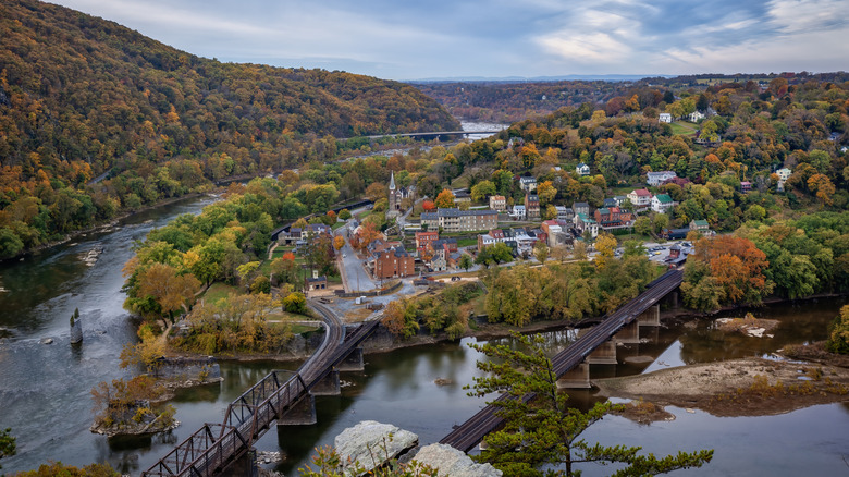 Scenic overview of the town of Harpers Ferry, West Virginia, with railroad bridges, town center, and mountains in the background