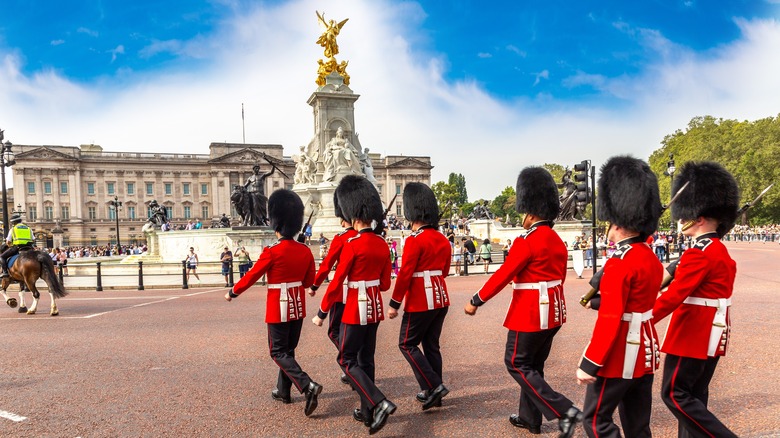 British soldiers in red uniforms and black furry hats walk near Buckingham Palace in London