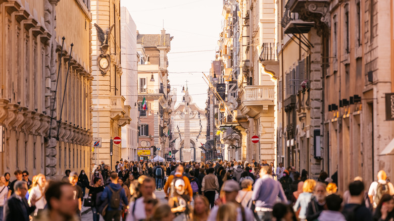 Narrow, ornate balcony-lined pedestrian street filled with crowds of people