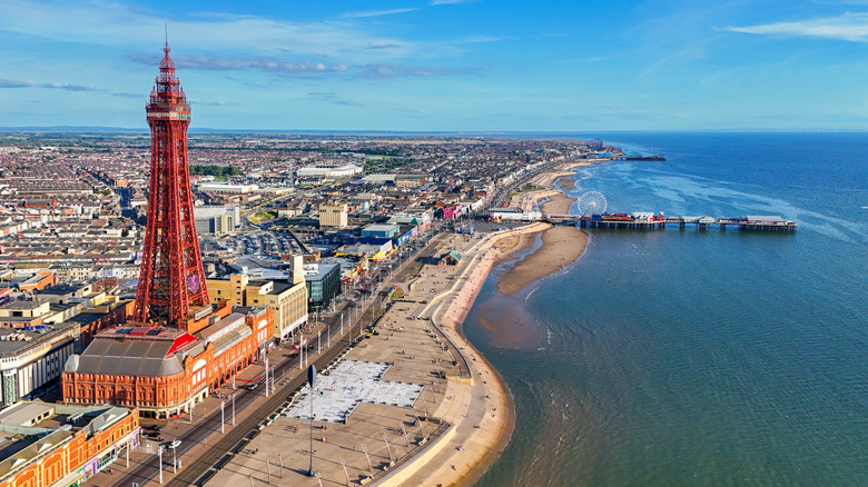 Aerial view of Blackpool with the red tower in the foreground and two seaside piers in the distance