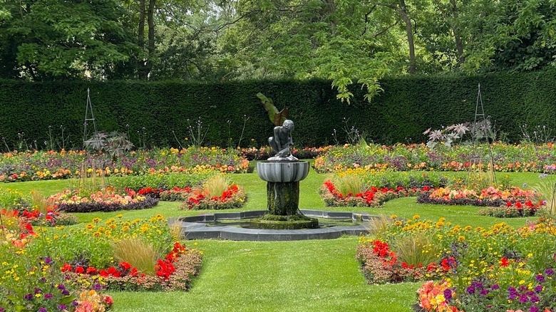Fountain flanked by colorful flowers with a tall hedge in the background at Queen Mary's Rose Garden, London