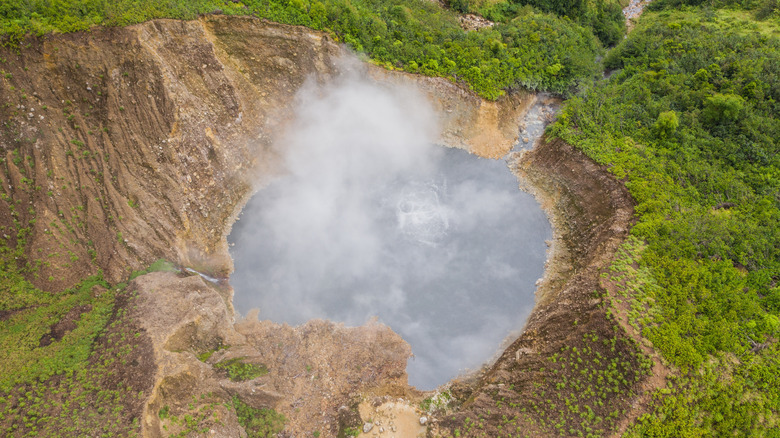 Steam rises from a water-filled crater surrounded by greenery at Boiling Lake, Dominica
