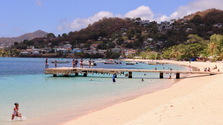 People swimming, sunbathing, and standing on a pier at Grand Anse Beach
