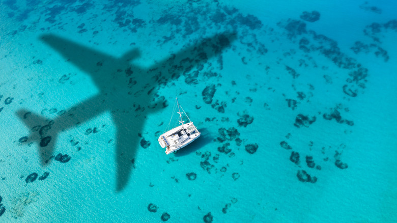 An airplane silhouette over a catamaran in clear turquoise Caribbean water.
