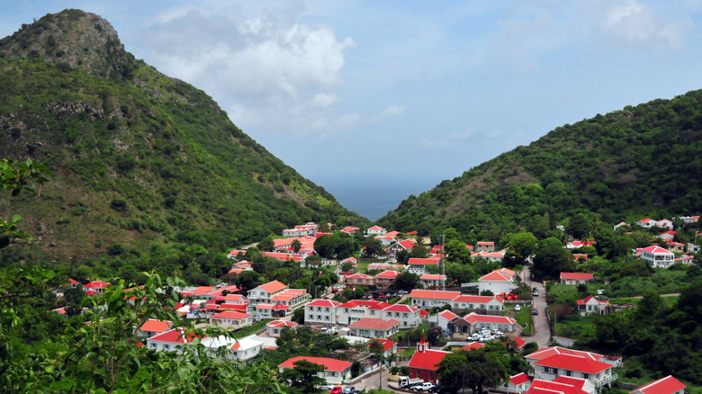 White buildings with red roofs nestled at the bottom of green-covered mountains