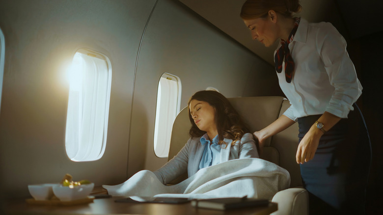 Flight attendant checking on a sleeping passenger