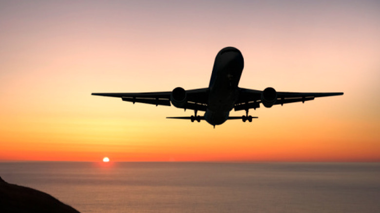 Plane taking off over an ocean at sunset