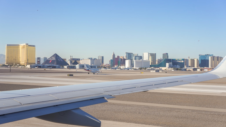 View from a passenger's perspective of the Harry Reid International Airport tarmac with an airplane wing in the foreground; the Las Vegas city skyline sits in the background