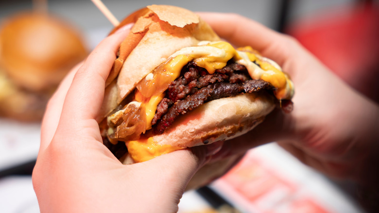 hands holding smash burger with cheese and onions