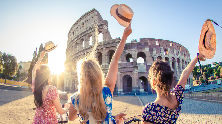 Three women wave their hats in front of the Colosseum in Rome, Italy