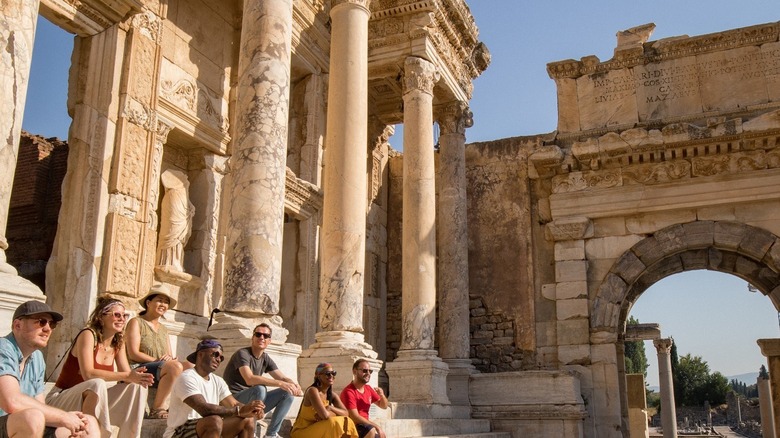 Tour group with guide sitting on ancient Greek ruins