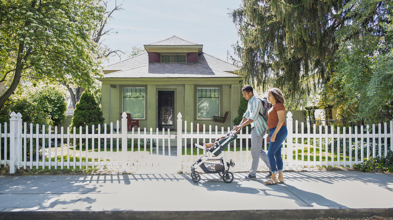 Parents pushing stroller past a bungalow