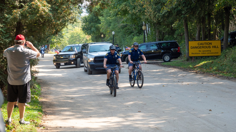 Law enforcement riding bicycles and a multi-vehicle motorcade driving on Mackinac Island, Michigan