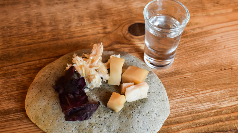 Cubes of plated hákarl shark next to a shot of liquor