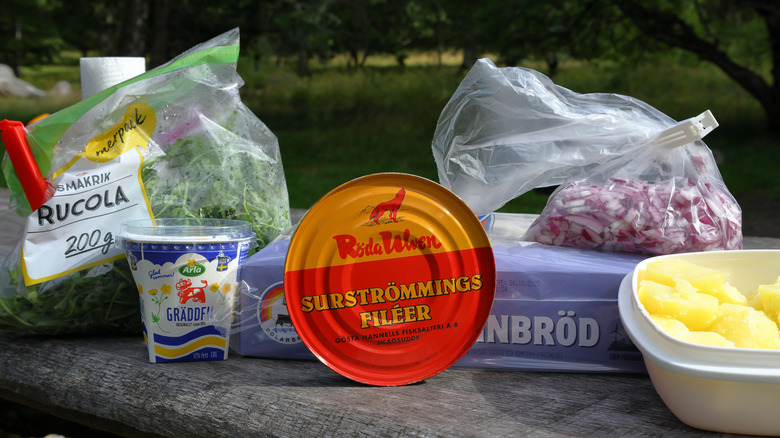 Can of surströmming next to potatoes, arugula, onion, and other ingredients
