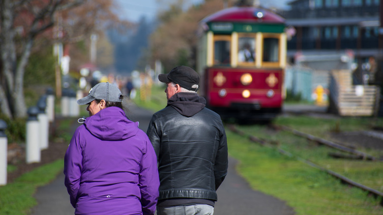 A couple walks along the Astoria Riverwalk as the Astoria Riverfront Trolley passes by