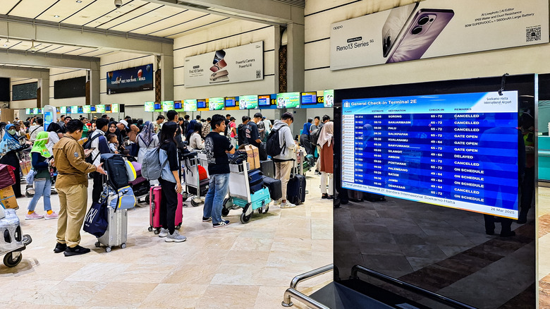 Passengers queue behind a screen showing canceled flights