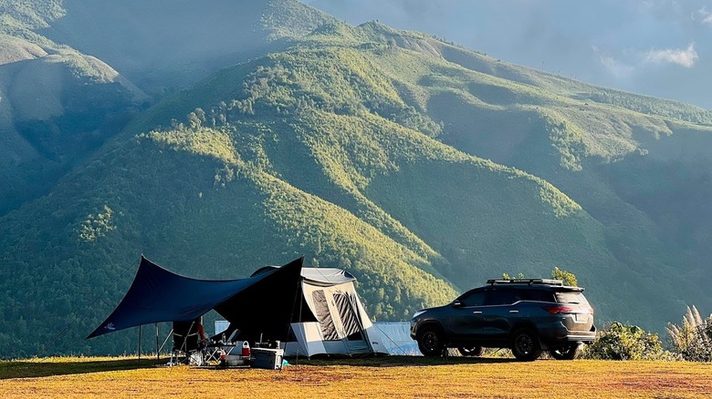 Tent and car in front of a lush green mountain