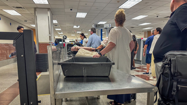 Passengers place luggage in security bins at an airport