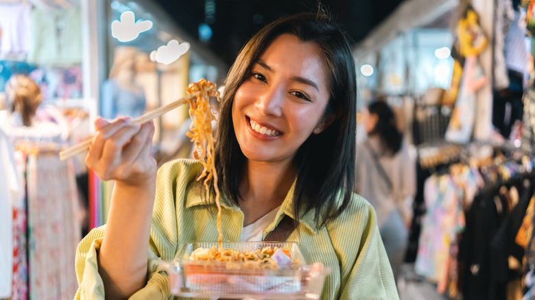 Asian woman enjoy eating noodles street food at night market in Thailand