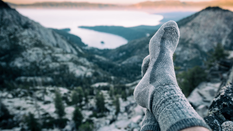 The feet of a hiker, covered in wool socks, propped up against a cliffside view
