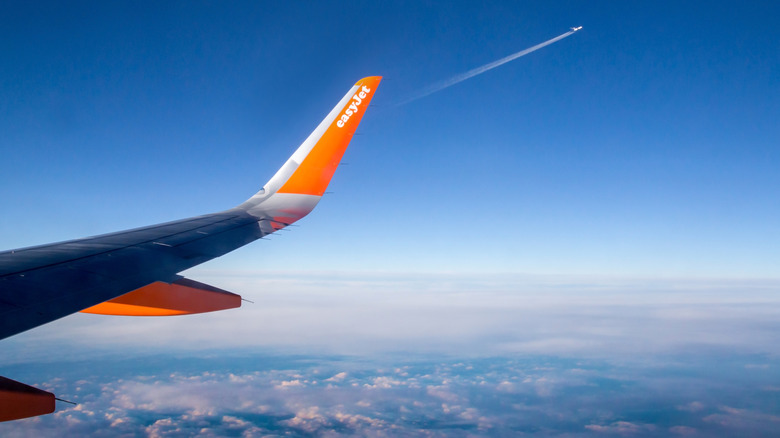 Orange and blue easyJet wing from a plane window, overlooking clouds