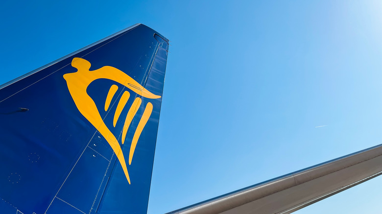 A blue wing of an airplane with a yellow Irish harp logo for Ryanair