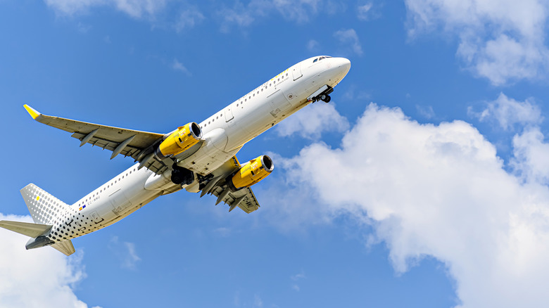 Looking up at a plane from Vueling in a blue partly cloudy sky