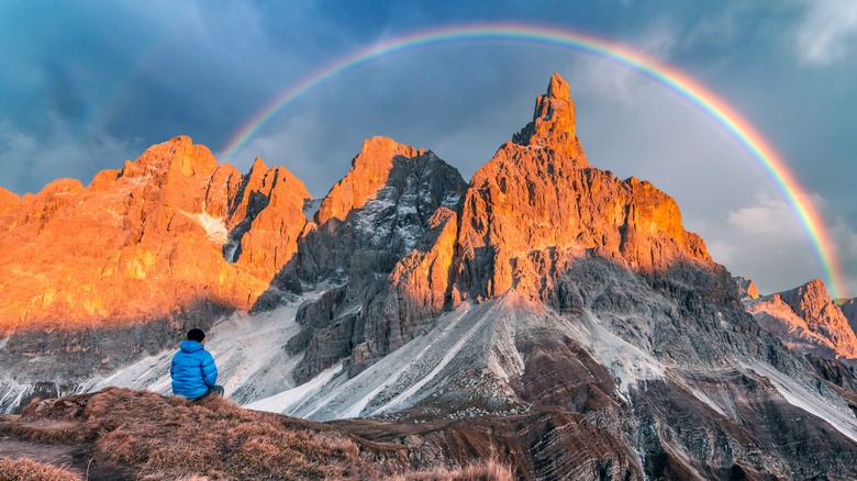 A hiker looks on at a rainbow over the Italian Dolomites