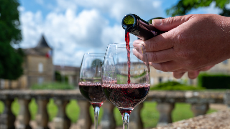 Hand pouring red Bordeaux wine into glasses on the grounds of a French chateau