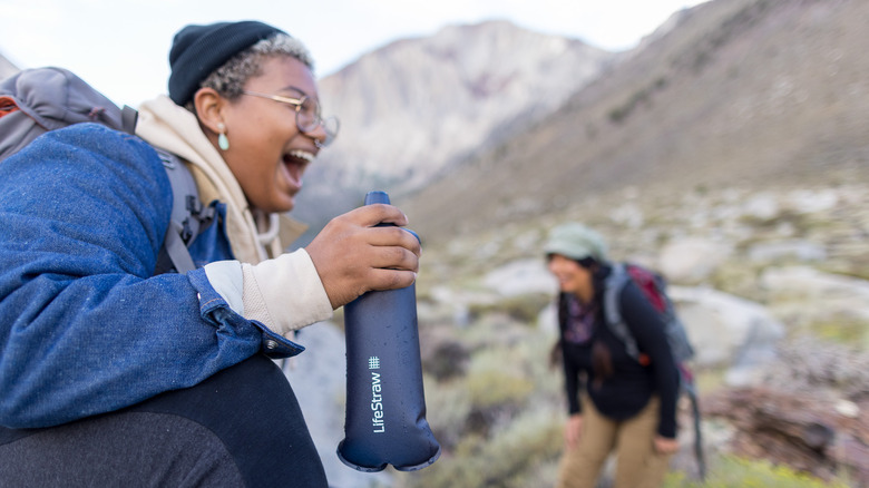 Two female hikers are laughing while one holds a LifeStraw Peak Series Collapsible Squeeze Bottle in her hand
