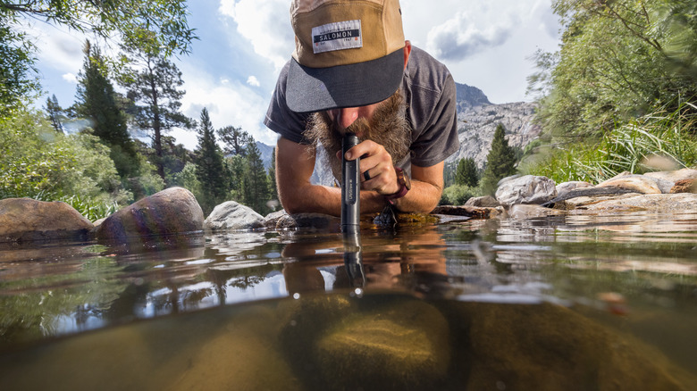 A man drinks water directly from a natural spring using a Peak Series LifeStraw