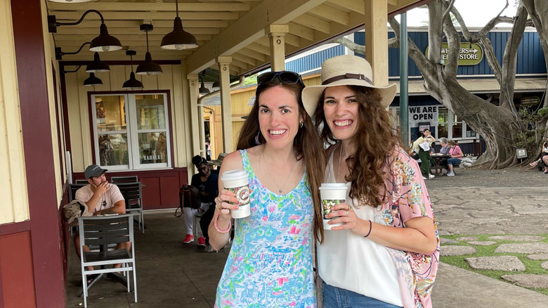 Two brunette women stand outside of Island Vintage coffee on Oahu's North Shore downtown strip holding coffee cups