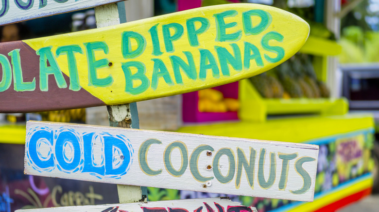 Colorful sign reading "chocolate dipped bananas" and "cold coconuts" at a downtown fruit stand, Hanalei, Hawaii