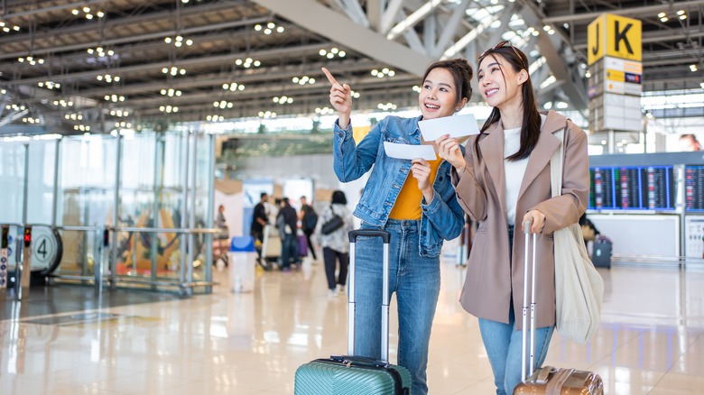 Two smiling women looking for their gate at the airport.