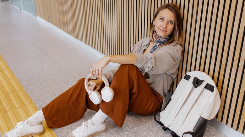 Woman wearing loose, brown pants while sitting on the airport floor.