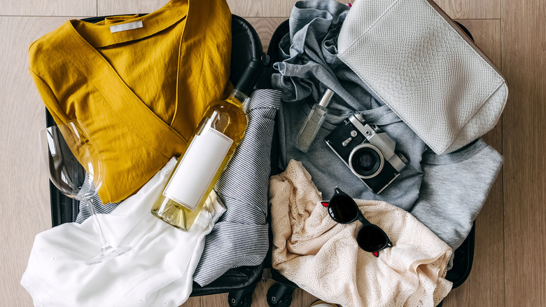 wine, a camera, clothes, and sunglasses in an open suitcase