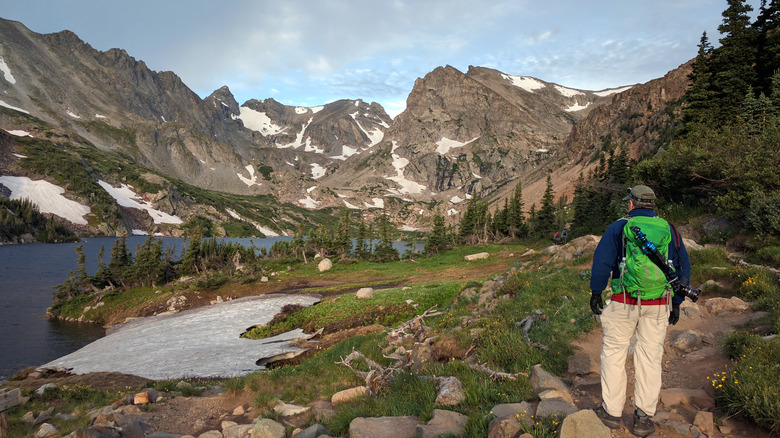 A hiker admiring a view of snowy mountains and an alpine lake in the Indian Peaks Wilderness, Colorado.
