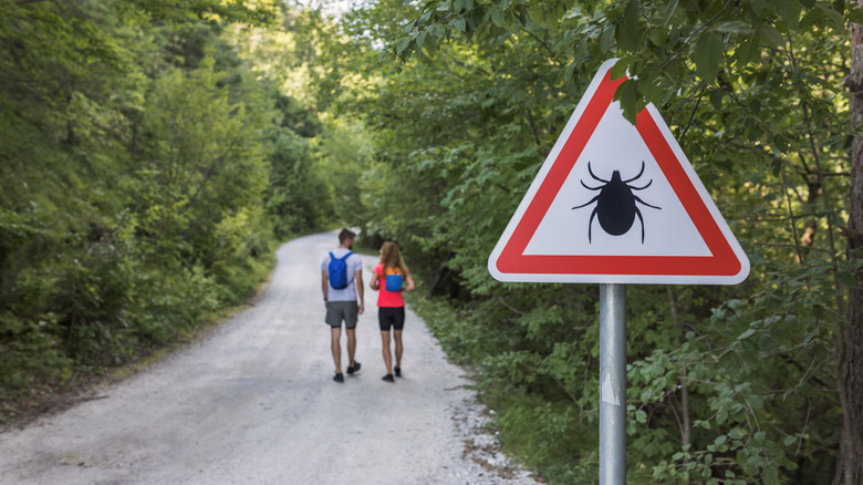 Couple hiking down the road with a danger of ticks sign in the foreground