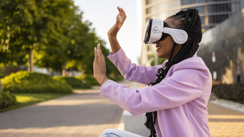 Women seated outside wearing a virtual reality headset and attempting to touch things she sees virtually
