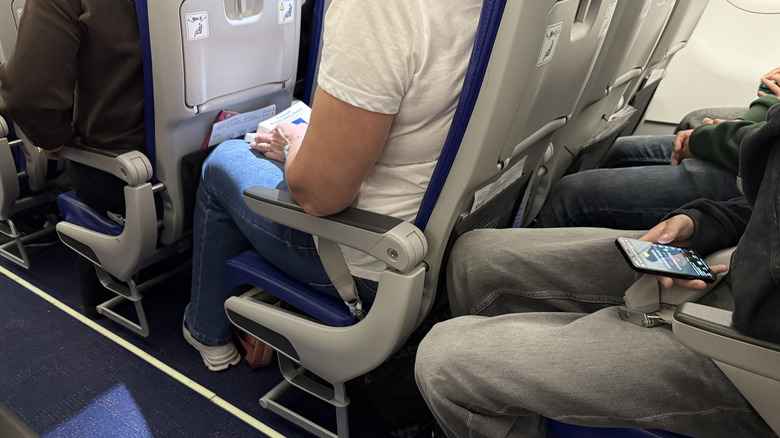 Close-up view of passengers from the shoulders down seated in tight economy seating on a plane