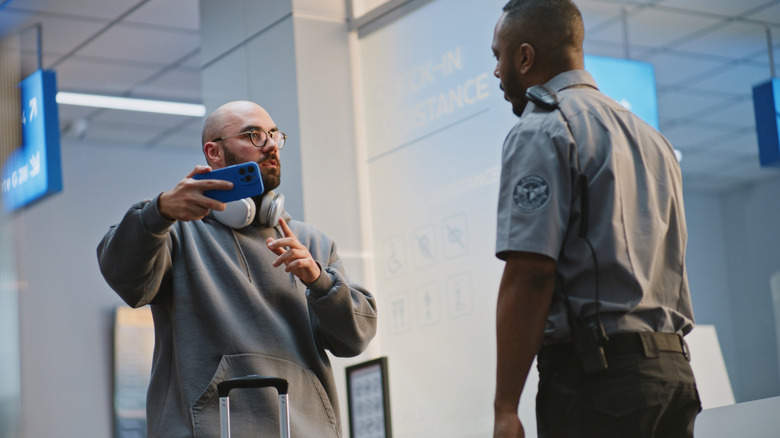 Man filming on smartphone being admonished by security personnel at an airport checkpoint