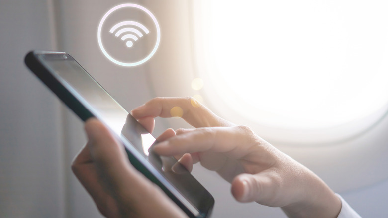 Woman's hand using smartphone with WiFi icon floating above phone with airplane background