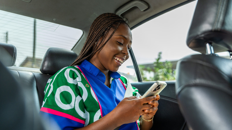 a smiling woman sits in the backseat on her phone